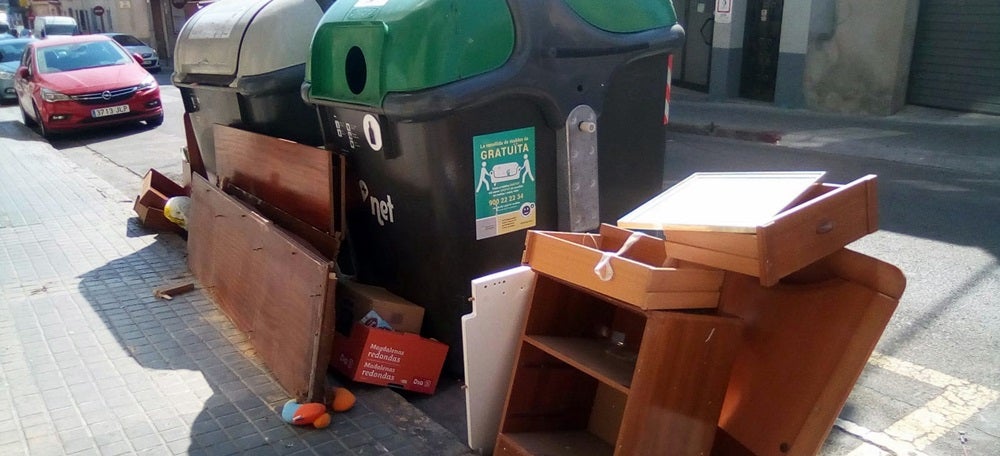 Muebles abandonados al lado de un contenedor. 