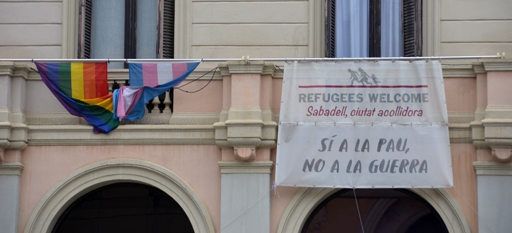 Foto portada: la bandera irisada i una a favor dels refugiants, a la plaça del doctor Robert. Autor: David B. 