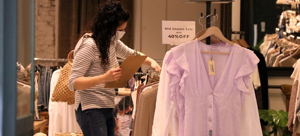 Pla mitjà d'una botiguera ordenant la roba en un establiment de Sabadell el 22 de març de 2020. (Horitzontal)