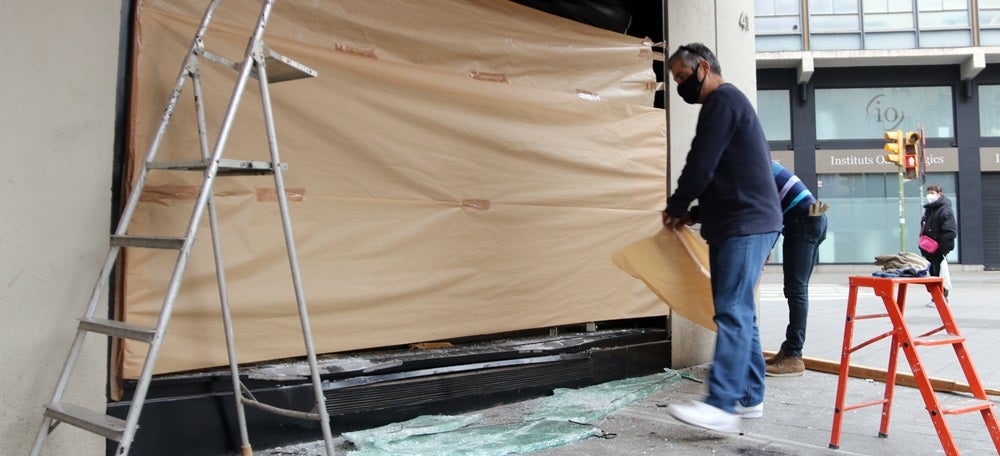 Pla general de dos operaris col·locant paper en una finestra a la joieria atracada al centre de Sabadell, el 18 de febrer de 2021. (Horitzontal)