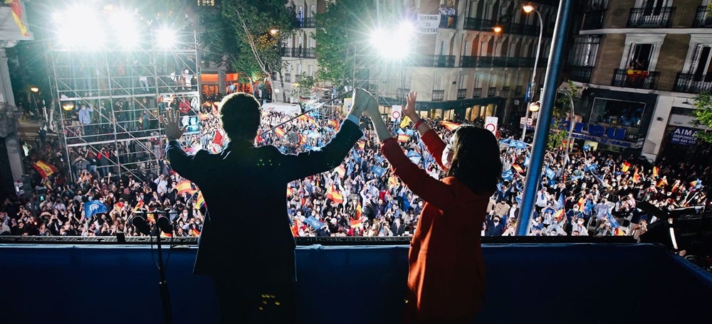 Foto portada: pla mitjà d'esquenes del president del PP, Pablo Casado, i de la guanyadora de les eleccions madrilenyes, Isabel Díaz Ayuso, al balcó de la seu del carrer Génova saludant els simpatitzants congregats, el 4 de maig de 2021 (horitzontal)