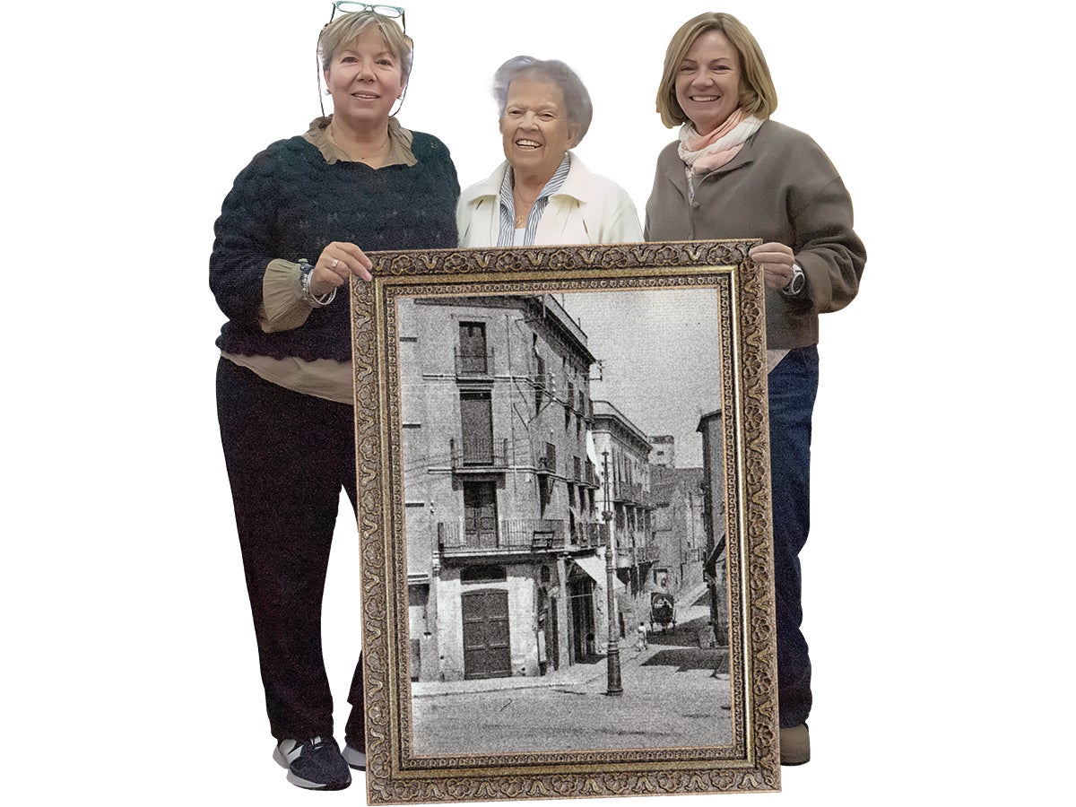 La Mariona i la Sílvia custodien a banda i banda la seva mare, la Roser. Totes tres, darrera d'una foto antiga on es veu el carrer de la merceria.