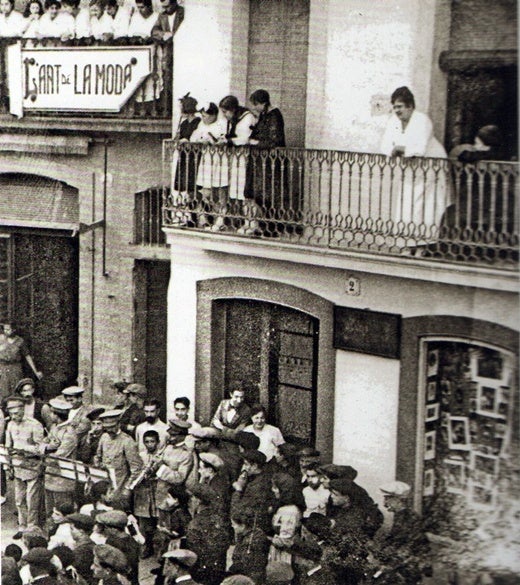 Banda Municipal tocant a la plaça de les Marquilles on es pot veure l'aparador de la botiga de Rifa i en el balcó la seva dona (1915). Autor desconegut/AFUES