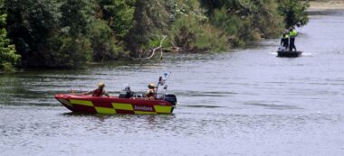 Primer pla del sostre dels vehicles d'emergències aparcats a la platja de l'Arenal de Miravet amb dues embarcacions de recerca buscant pel riu Ebre. Imatge del 3 de juny del 2021 (horitzontal)