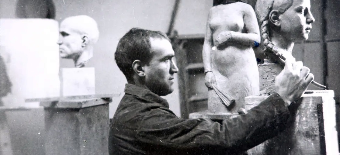 L’escultor Camil Fàbregas al seu taller, treballant en el bust de Cleopatra Burguès Padrós. Asseguda en un tamboret alt, fent de model, Cleopatra. Sabadell, 1934. Autor desconegut (AHS)