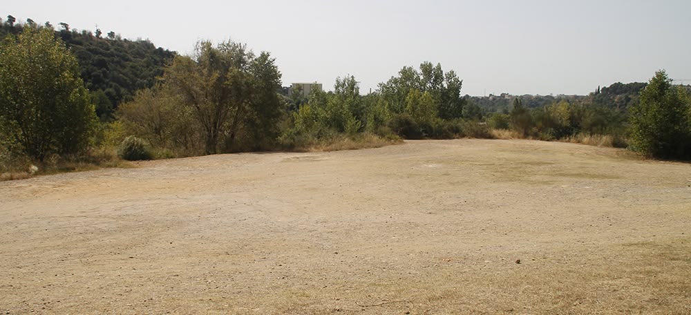 El solar on es vol construir una piscina d'onades, al costat de la Bassa, davant la Pista Coberta i darrera del riu Ripoll, el 5 de juliol. Autora: Lucía Marín.